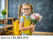 A pretty first-grader girl with glasses and ponytails on her head. In the hands of a bouquet of autumn flowers. The child goes to school for the first time. A child with a backpack, a book and flowers. Back to school. Стоковое AI-изображение, AI-художник Photojuli / Фотобанк Лори