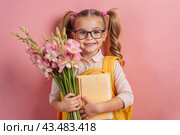 A pretty first-grader girl with glasses and ponytails on her head. In the hands of a bouquet of autumn flowers. The child goes to school for the first time. A child with a backpack, a book and flowers. Back to school. Стоковое AI-изображение, AI-художник Photojuli / Фотобанк Лори