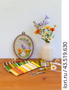 Summer still life with handmade floral embroidery with satin ribbons of flowers in hoop. Bouquet of daisies, marigolds and blue bells on wooden table. Crafts and embroidery as hobby. DIY concept. Стоковое фото, фотограф Виктория Катьянова / Фотобанк Лори