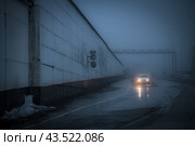 The car drives down a dark unlit street. View of the road and a high concrete fence. Bright light of car headlights at dusk. Gloomy mood. Стоковое фото, фотограф Андрей Степанов / Фотобанк Лори