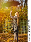Attractive happy woman in a gray coat holds an umbrella in her hands. Leaf fall in the autumn park. Beautiful young woman is walking among the falling leaves. Yellow foliage. Fall season. Autumn mood. Стоковое фото, фотограф Андрей Степанов / Фотобанк Лори