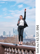 Girl sings standing on balustrade enclosing observation deck on Sparrow hills, Moscow, Russia (2024 год). Редакционное фото, фотограф Ирина Кононова / Фотобанк Лори