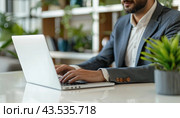 A man with a beard, wearing a hat, is seated at a table, working on his laptop computer. Стоковое AI-изображение, AI-художник Юрий Поздников / Фотобанк Лори