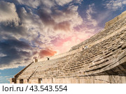 Roman Theatre in Amman, Jordan -- theatre was built the reign of Antonius Pius (138-161 CE), the large and steeply raked structure could seat about 6000 people. Against the sky with clouds (2016 год). Стоковое фото, фотограф Владимир Журавлев / Фотобанк Лори