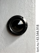 Close-up of black lens peephole on white metal door, glare on lens. Circular eye window with a black frame and circular glass pane on white wall. Security and safety concept. Copy ad text space. Стоковое AI-изображение, AI-художник Aleksandr Golubev / Фотобанк Лори