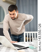 Man experiencing severe back pain after working long hours on laptop. Стоковое фото, фотограф Яков Филимонов / Фотобанк Лори