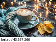 A seasonal drink. Delicious hot cappuccino in a mug with a saucer and a knitted snood, a scarf on a wooden table in the interior of the cafe. It's a rainy autumn day. Стоковое AI-изображение, AI-художник Photojuli / Фотобанк Лори
