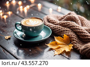 A seasonal drink. Delicious hot cappuccino in a mug with a saucer and a knitted snood, a scarf on a wooden table in the interior of the cafe. It's a rainy autumn day. Стоковое AI-изображение, AI-художник Photojuli / Фотобанк Лори
