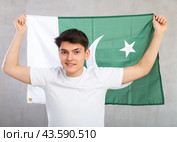 Happy young man holding flag of Pakistan against unicoloured background. Стоковое фото, фотограф Яков Филимонов / Фотобанк Лори