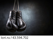 Professional black boxing gloves hang on a black background with a space to copy. Стоковое AI-изображение, AI-художник Photojuli / Фотобанк Лори