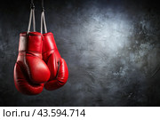 Professional red boxing gloves hang on a black background with a space to copy. Стоковое AI-изображение, AI-художник Photojuli / Фотобанк Лори