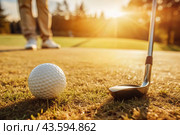 The banner. A white ball and a metal golf club are lying on the lawn in the hands of a man against the sunset background. An advertisement for a golf game at a country club. Free space for text. Стоковое AI-изображение, AI-художник Photojuli / Фотобанк Лори