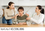 Sad woman sits silently in kitchen, adult girls sympathize and comfort her. Стоковое фото, фотограф Яков Филимонов / Фотобанк Лори
