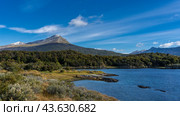 The beautiful landscape of Patagonia in autumn. A green forest and yellowed grass grow on the shore of a blue lake. Snow-capped mountain against a sky and clouds. Lapataia Bay. Tierra del Fuego. Стоковое фото, фотограф Вера Ивановна Кубарева / Фотобанк Лори