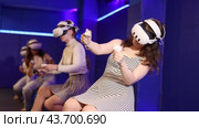 Four cheerful emotional young female friends in VR goggles sitting in virtual reality room, manipulating objects or shooting at targets with gaming controllers in hands. Стоковое видео, видеограф Яков Филимонов / Фотобанк Лори
