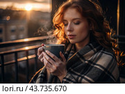 A red-haired, beautiful woman wrapped in a plaid with a mug of hot coffee on a beautiful patio in the rays of the setting sun. The girl inhales the aroma of the drink. Comfort and harmony. Стоковое AI-изображение, AI-художник Photojuli / Фотобанк Лори