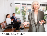 Friendly mature woman stands at office reception with list of guests and expects invited visitors. Стоковое фото, фотограф Яков Филимонов / Фотобанк Лори