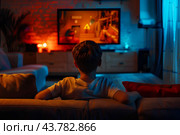 Мальчик сидит один в темной комнате, смотрит кино по телевизору. Стоковое AI-изображение, AI-художник Щеголева Ольга / Фотобанк Лори