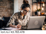 A young female freelance businessman in glasses and headphones is working on a laptop or shopping in an online store. The woman is writing something in a notebook. Стоковое AI-изображение, AI-художник Photojuli / Фотобанк Лори