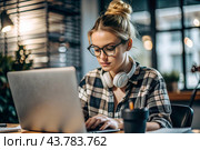 A young female freelance businessman in glasses and headphones is working on a laptop or shopping in an online store. The woman is writing something in a notebook. Стоковое AI-изображение, AI-художник Photojuli / Фотобанк Лори