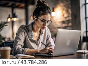 A young female freelance businessman in glasses and headphones is working on a laptop or shopping in an online store. The woman is writing something in a notebook. Стоковое AI-изображение, AI-художник Photojuli / Фотобанк Лори