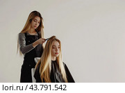 A female hairdresser makes a fashionable hairstyle for a blonde girl. Copy space. Стоковое AI-изображение, AI-художник Ярославский Максим / Фотобанк Лори