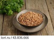 Boiled buckwheat porridge in black bowl on dark old wooden background, side view. Стоковое фото, фотограф Natalia Gdovskaia / Фотобанк Лори