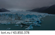An endless field of blue ice stretches to the horizon. Cracks, sharp peaks. Melted ice floes float in the turquoise water of a glacial lake. Coastal mountains in clouds and fog. Perito Moreno. Стоковое фото, фотограф Вера Ивановна Кубарева / Фотобанк Лори