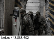 Группа военных в камуфляже выстроилась за солдатом с бронещитом и пистолетом и входит в помещение. Штурм и зачистка. Стоковое фото, фотограф Евгений Зимин / Фотобанк Лори