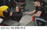 A young female athlete performs an exercise with a gym ball under the supervision of a coach. Fitness class with an experienced trainer in the gym. Стоковое видео, видеограф Енваев Андрей / Фотобанк Лори