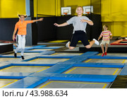 Full length of excited casual schoolchild girl having fun while jumping high on colorful trampoline at game club. Стоковое фото, фотограф Яков Филимонов / Фотобанк Лори