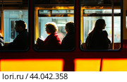 People sitting inside a transit vehicle illuminated by sunlight during the afternoon in an urban setting. Стоковое AI-изображение, AI-художник Сергей Толмачёв / Фотобанк Лори