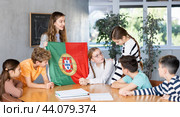 Female teacher, conducting extracurricular lesson in the school class tells schoolchildren the history of Portugal and shows national flag of country. Стоковое фото, фотограф Яков Филимонов / Фотобанк Лори