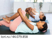 Children doing yoga with group in studio, lying on mat with knee pressed to chest with hands, performing hamstring and low back stretching Ardha Pawanmuktasana. Стоковое фото, фотограф Яков Филимонов / Фотобанк Лори
