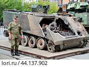 Российский военнослужащий возле разбитого американского бронетранспортера M113 A2. Выставка трофейной техники из зоны СВО. Город Тюмень (2024 год). Редакционное фото, фотограф Александр Тараканов / Фотобанк Лори