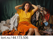 Young woman sits exhausted amidst a pile of colorful, unfolded laundry. Стоковое AI-изображение, AI-художник Иван Рябоконь / Фотобанк Лори