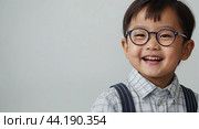 Portrait of a happy Asian kid preschooler with glasses on a solid gray background. Back to school, correction of pupil kid eyesight. AI generated. Стоковое AI-изображение, AI-художник Ольга Симонова / Фотобанк Лори