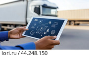 A truck driver checks routing and logistics information on a tablet while parked in a transportation yard, surrounded by trucks under a clear sky. Стоковое AI-изображение, AI-художник Liliia Kanunnikova / Фотобанк Лори