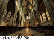 Symmetrical view of a gothic cathedral's nave with soaring arches and stained glass. Стоковое AI-изображение, AI-художник Иван Рябоконь / Фотобанк Лори