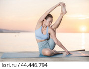 Sports experienced woman yoga teacher performs compass pose, parivritta surya yantrasana on mat on beach at sunset. Стоковое фото, фотограф Яков Филимонов / Фотобанк Лори