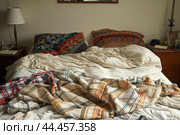 Unmade bed with cozy blankets in morning light. Стоковое AI-изображение, AI-художник Иван Рябоконь / Фотобанк Лори