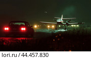 A vintage car parked on a dimly lit airstrip while a small aircraft prepares for takeoff at night. Стоковое AI-изображение, AI-художник Сергей Толмачёв / Фотобанк Лори