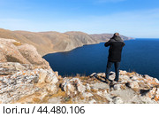 Lake Baikal on sunny autumn day. Tourist takes a photo of lake's water landscape from coastal steep cliffs. View of endless expanse of blue water and mountains and hills without forest of Tazheran steppe. Стоковое фото, фотограф Виктория Катьянова / Фотобанк Лори