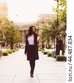 Beautiful serious smart brunette girl holding cup of coffee in hands goes walking down street of St. Petersburg in city center. Charming thoughtful woman with long dark hair wanders alone. Стоковое фото, фотограф Natalia Gdovskaia / Фотобанк Лори