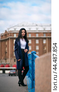 Charming thoughtful fashionably dressed woman with long dark hair travels through Europe, standing in city center of St. Petersburg. A beautiful girl wanders alone through autumn streets. Стоковое фото, фотограф Natalia Gdovskaia / Фотобанк Лори