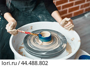 Unrecognisable woman making ceramic pottery on wheel, paints blue. Concept for woman in freelance, business. Handcraft product. Earn extra money, side hustle, turning hobbies into cash. Стоковое фото, фотограф Natalia Gdovskaia / Фотобанк Лори