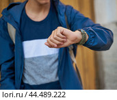 Young adult looks at the clock, waiting for a meeting with friends. A man is waiting for a woman in a street of city on a date, looking at watch. Стоковое фото, фотограф Natalia Gdovskaia / Фотобанк Лори