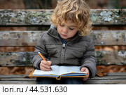 Young child concentrating on writing in notebook outdoors. Стоковое AI-изображение, AI-художник Иван Рябоконь / Фотобанк Лори