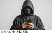 Hacker wearing a black mask and using a smartphone. Стоковое AI-изображение, AI-художник Юрий Поздников / Фотобанк Лори