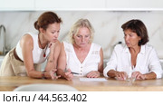 Three women help each other sort out financial documents in the kitchen of a home. Стоковое видео, видеограф Яков Филимонов / Фотобанк Лори